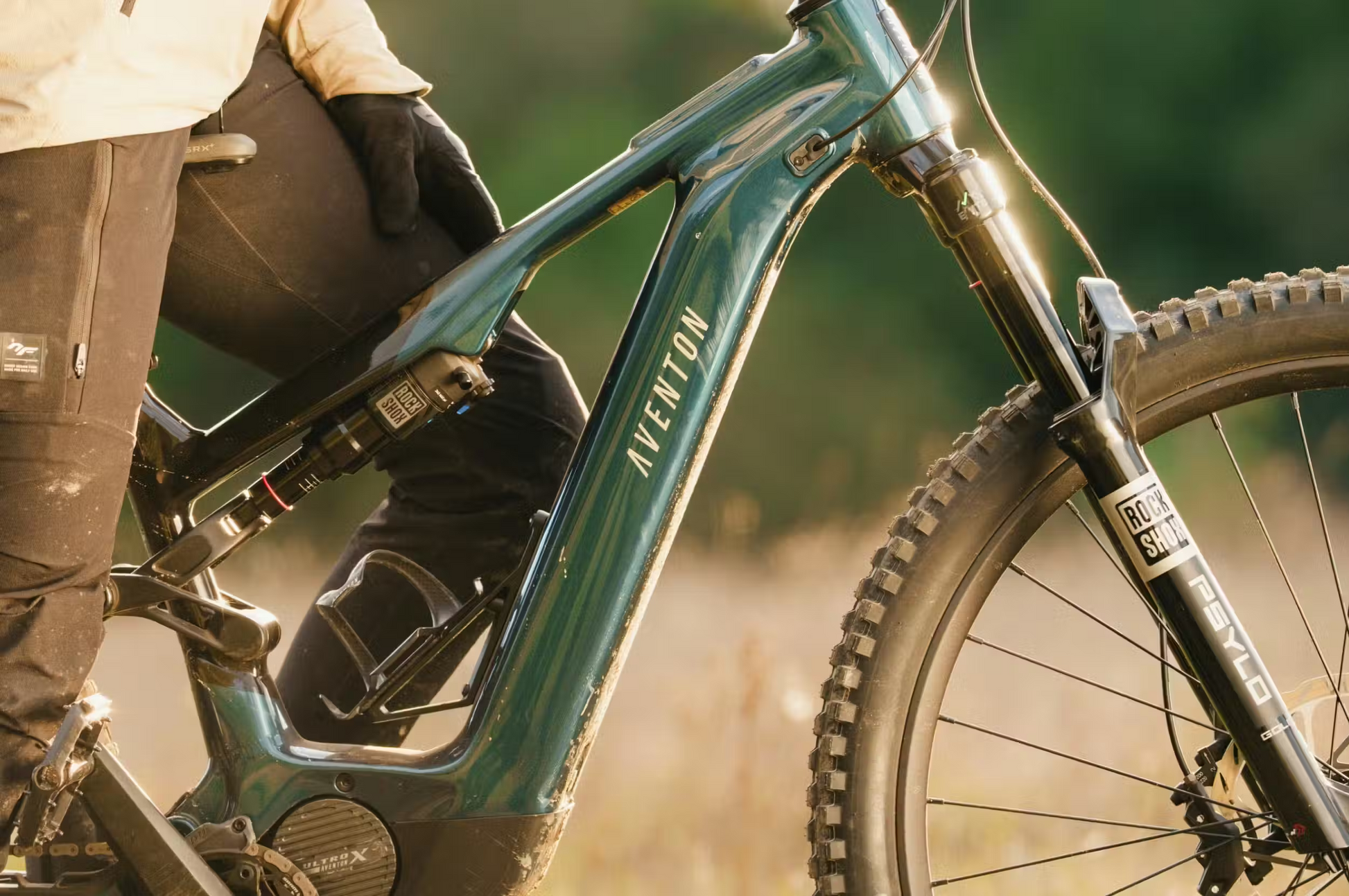 Close-up of a person in gloves and outdoor gear sitting on the Aventon Current ADV by Aventon, a full-suspension eMTB, outdoors in natural light.
