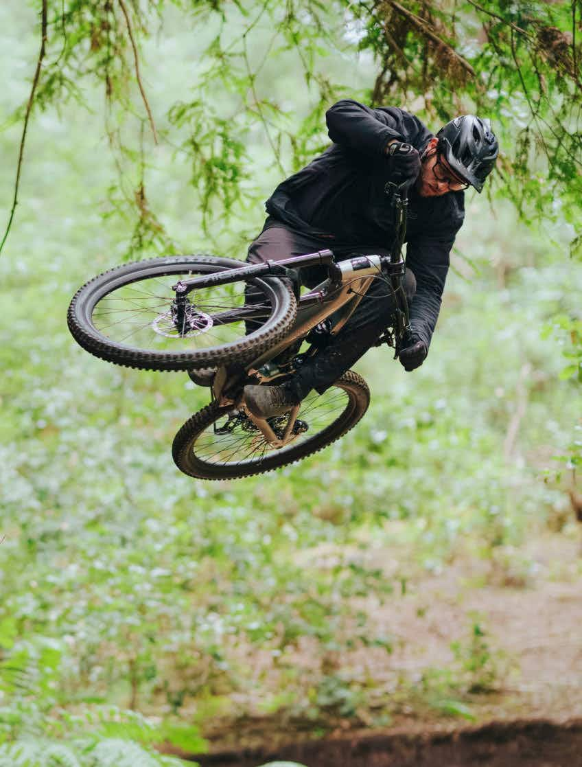 A rider in a helmet and dark clothing jumps through a forest on the Aventon Current EXP carbon eMTB by Aventon.