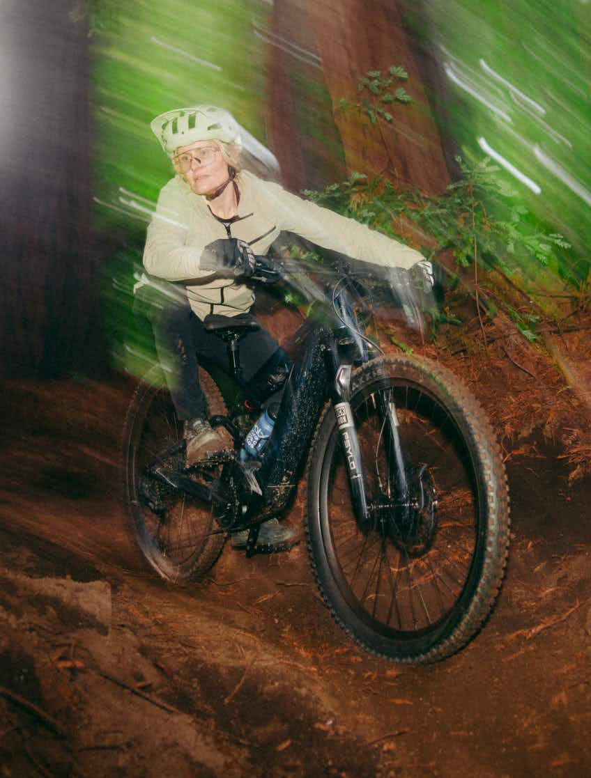 A rider wearing a helmet rides the Aventon Current EXP, a carbon eMTB by Aventon, through a forest trail at night with motion blur in the background.