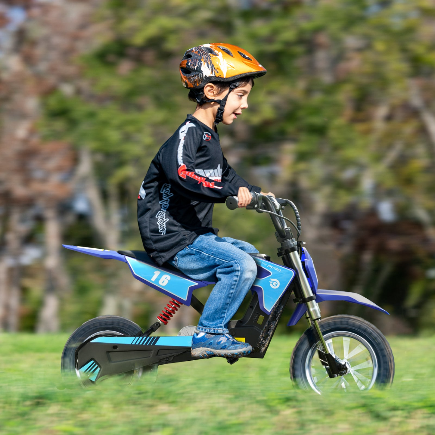 A young boy wearing a helmet rides a blue Hiboy DK1 Electric Dirt Bike on grass, with blurred trees in the background.