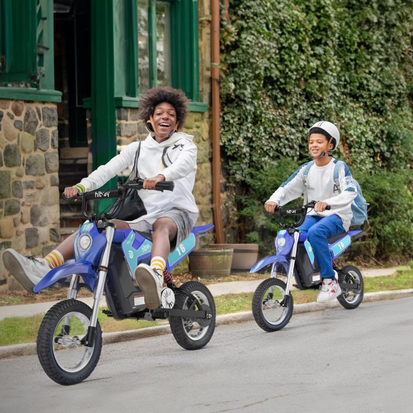 Two kids ride Hiboy - DK1 Electric Dirt Bikes by Hiboy on a residential street, both smiling in casual clothes; one child wears a helmet and backpack.