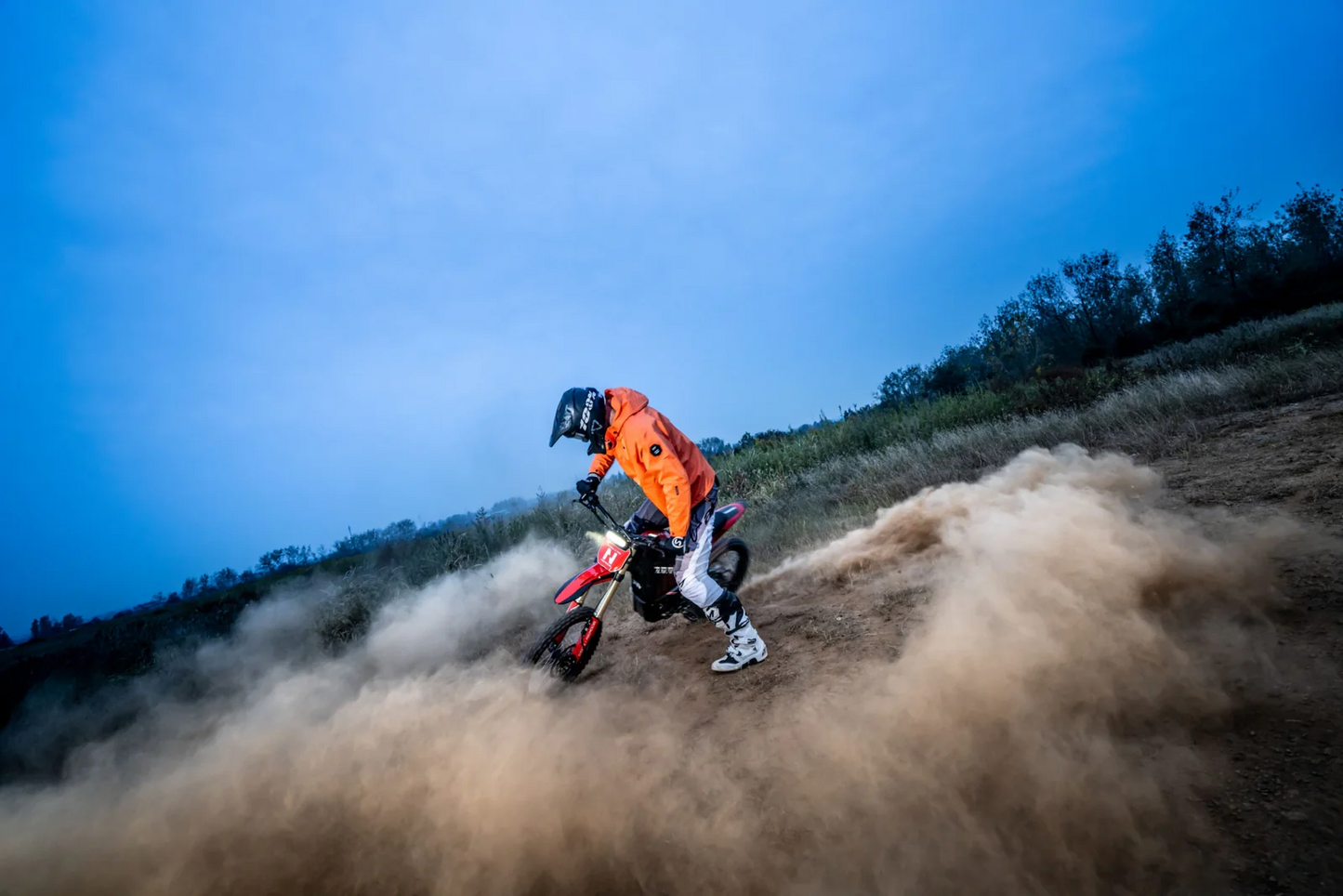 A person in an orange jacket rides the Navee Storm X Pro electric dirt bike by Navee, featuring a 17KW mid-drive motor, along a dusty trail under a blue sky, kicking up a large cloud of dust.
