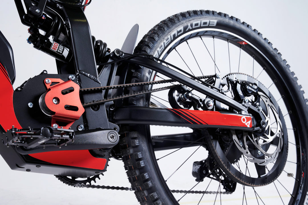 Close-up of a high-tech mountain bike's rear wheel and suspension system, featuring a belt drive, disc brakes, and shock absorber against a plain white background. The setup is enhanced by LMX's LMX - 64 brushless mid-mounted motor for reliable pedal assistance.