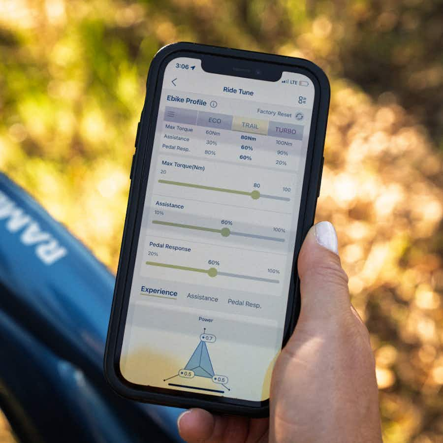 A person holds a smartphone showing an e-bike tuning app with adjustable assist, torque, and pedal settings—ideal for customizing the Aventon Ramblas ADV electric mountain bike by Aventon with its mid-drive motor.