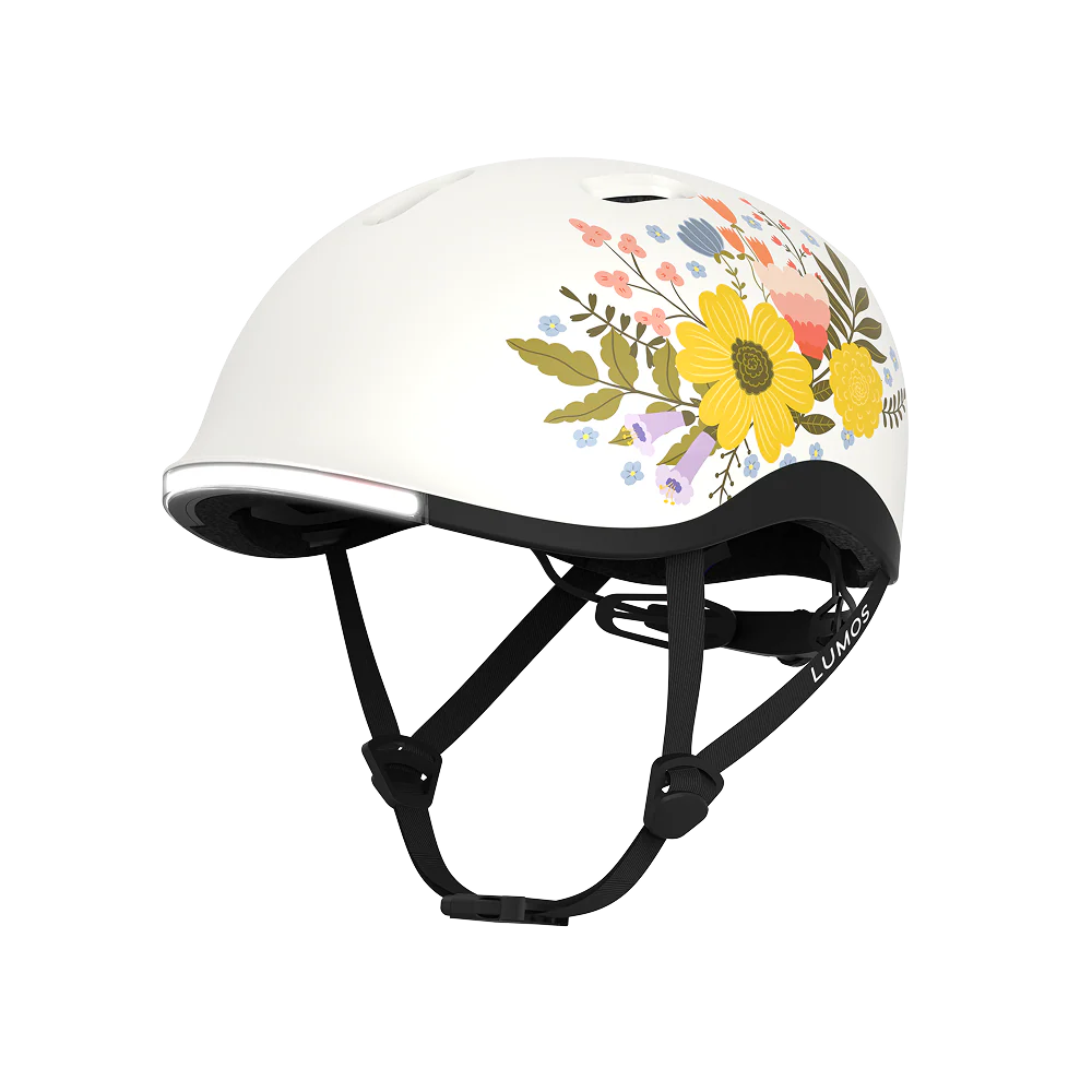 The Lumos NYXEL helmet is a white high-visibility model with black straps, decorated on the side with a floral design featuring yellow, pink, and purple flowers plus green leaves.