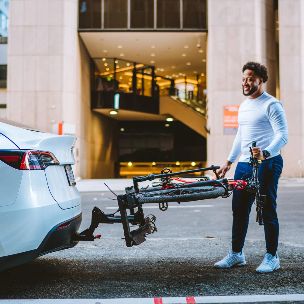 A man standing next to a Hollywood Racks - Destination eBike Rack with a bicycle attached to it using a hitch bike rack.