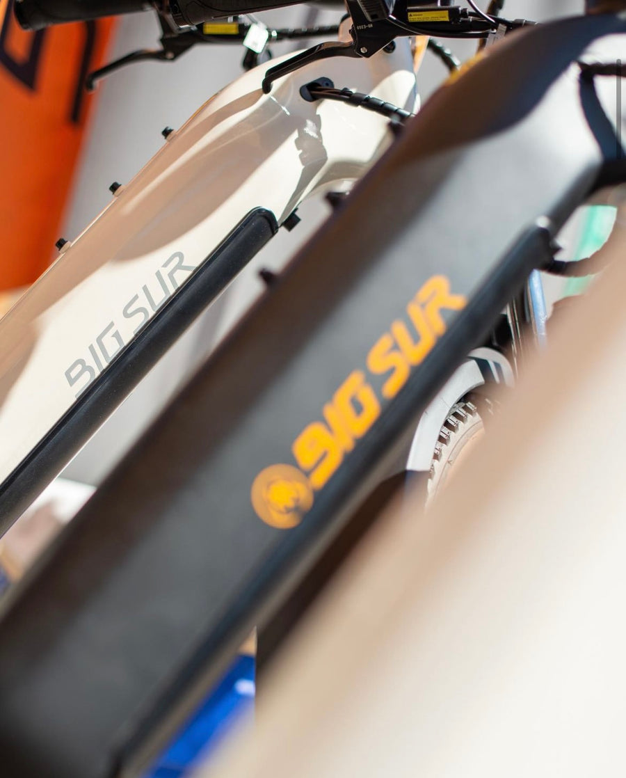 Close-up of two bicycles featuring the branding "AIMA - Big Sur" with "AIMA" and "910 SUR" in orange and white text, highlighting their all-terrain design.