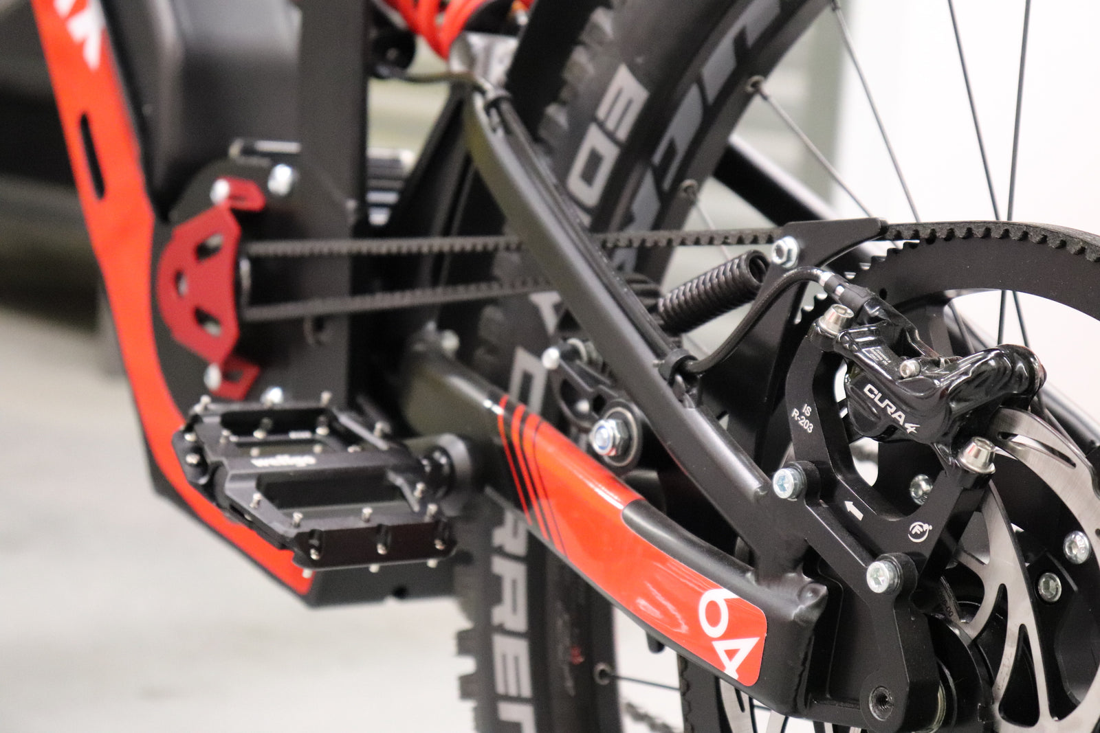 Close-up image of a bicycle drivetrain featuring a belt drive, rear derailleur, and pedals with a black and red color scheme from LMX, highlighting the brushless mid-mounted motor for optimal pedal assistance on the LMX - 64.