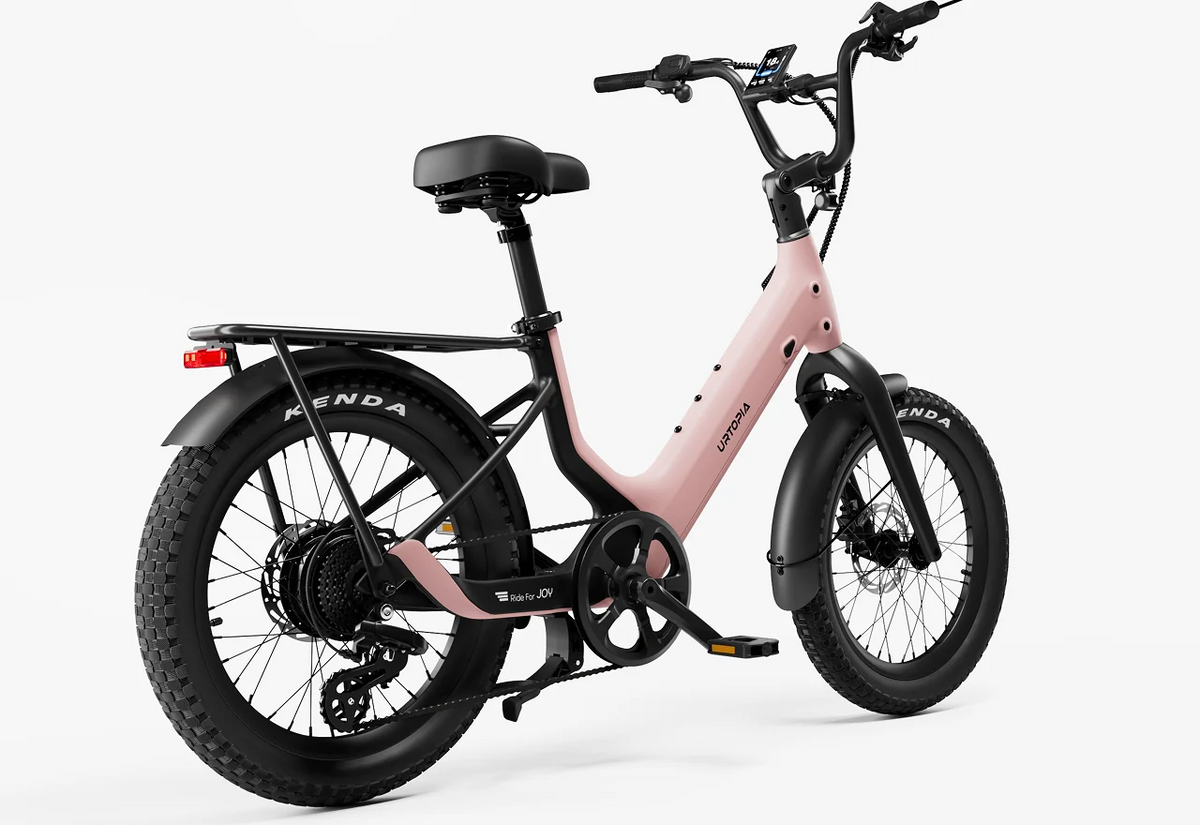 A Urtopia Carbon Joy Ultra electric cruiser bicycle by Urtopia, featuring a pink and black color scheme, thick tires, front and rear fenders, a step-through frame, rear cargo rack, and digital display, displayed on a white background.
