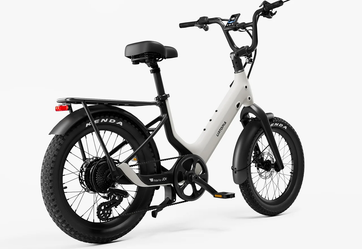 The Urtopia - Carbon Joy Ultra by Urtopia, an electric cruiser e-bike featuring a white step-through frame, fat tires, rear cargo rack, and fenders, is displayed from a rear side angle against a plain background.