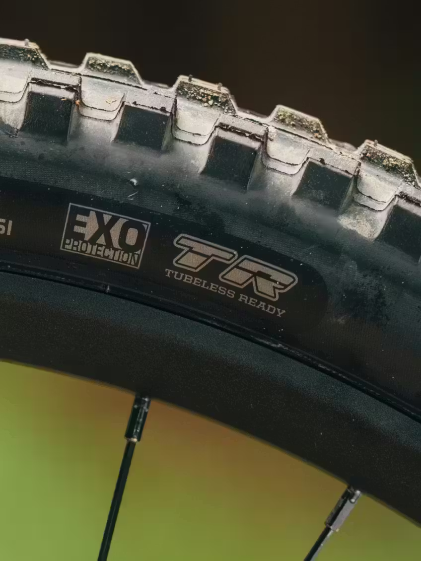 Close-up of an Aventon Current ADV electric mountain bike tire, showing tread pattern, sidewall branding with "EXO Protection" and "Tubeless Ready" labels, plus part of the rim and spokes—perfect for Aventon's full-suspension eMTB.
