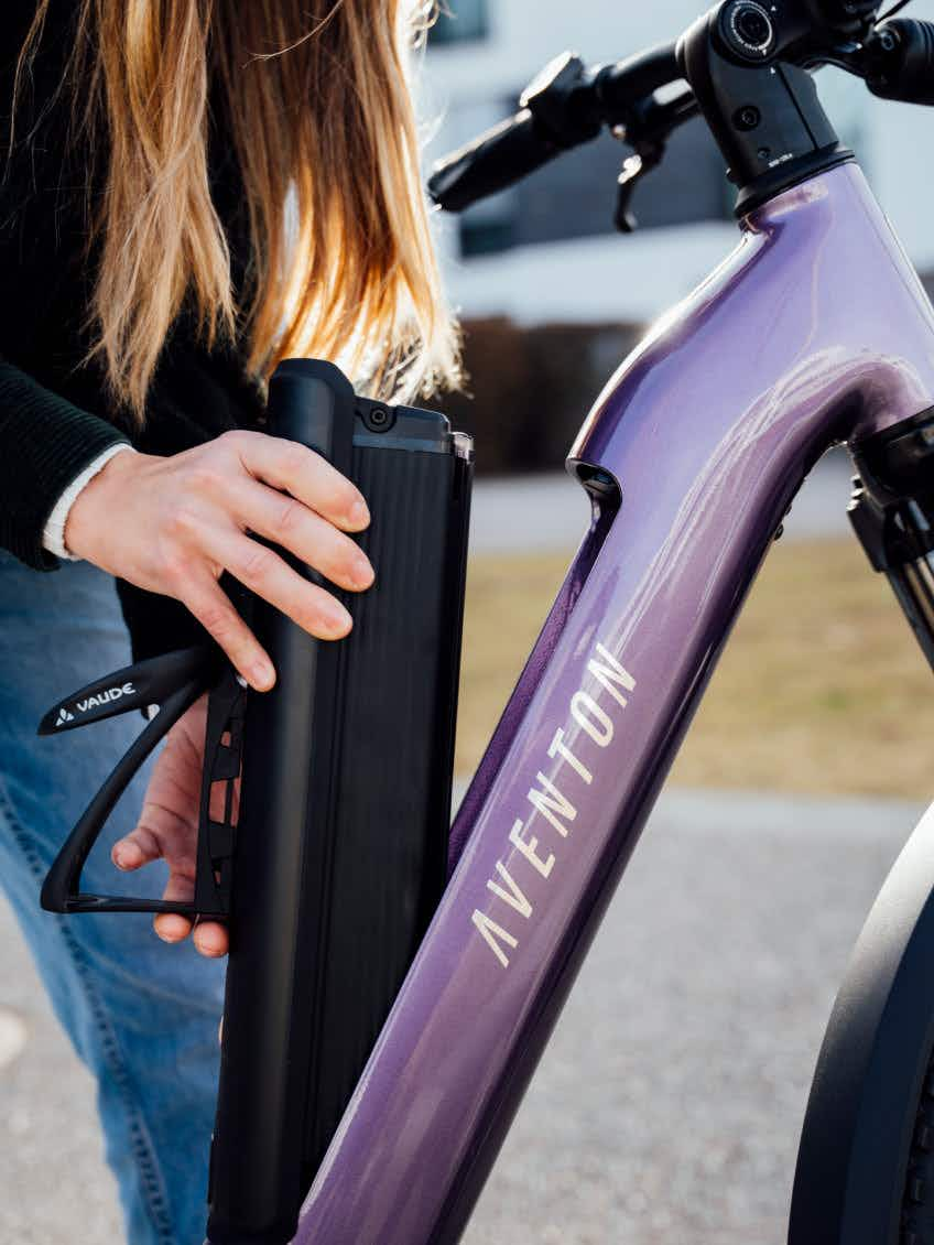 Someone detaches the battery from the frame of a purple Aventon Level 4 ADV eBike by Aventon.
