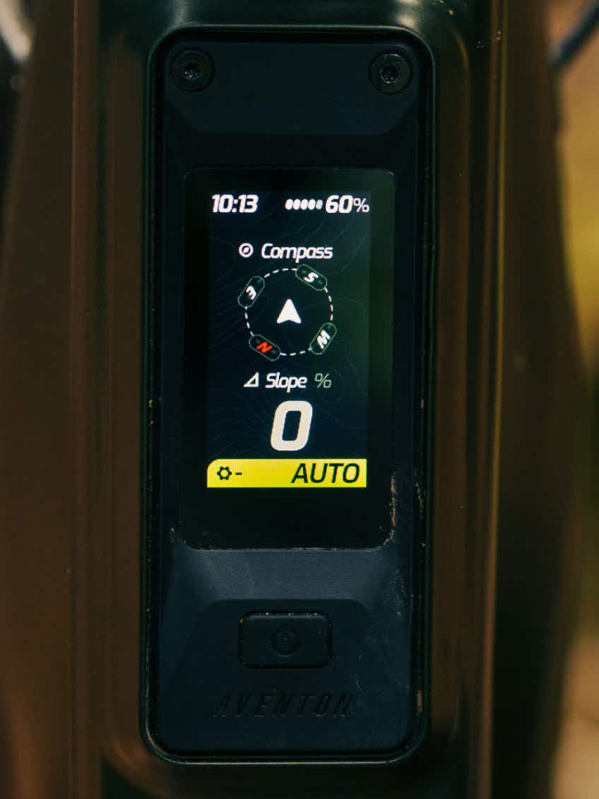Close-up of an Aventon Current EXP display showing time, battery at 60%, compass, slope at 0%, and auto mode on.