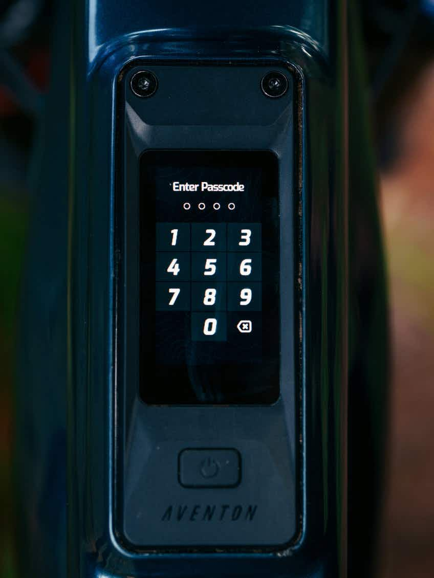 Close-up of an electronic keypad display on the Aventon Current EXP electric mountain bike by Aventon, showing a passcode entry screen with numbers 0–9 visible.