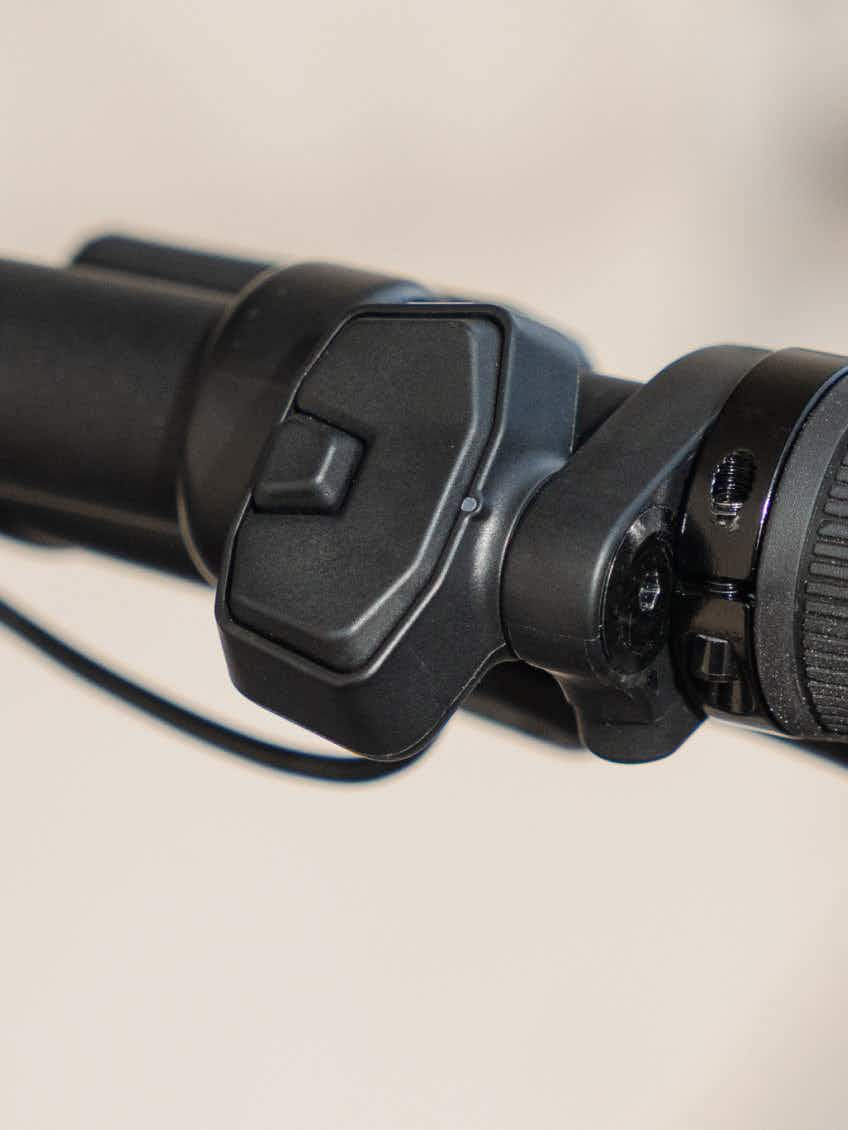 Close-up of a black handlebar-mounted control switch with a rectangular button and visible wiring, attached to the cylindrical bar of the Aventon Level 4 ADV electric bike by Aventon.