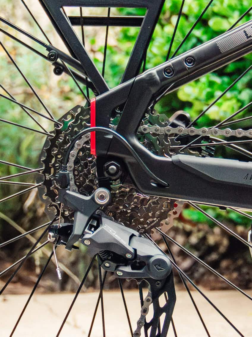 Close-up of the Aventon Level 4 ADV’s rear derailleur, cassette, and disc brake system by Aventon, set against a blurred green background.