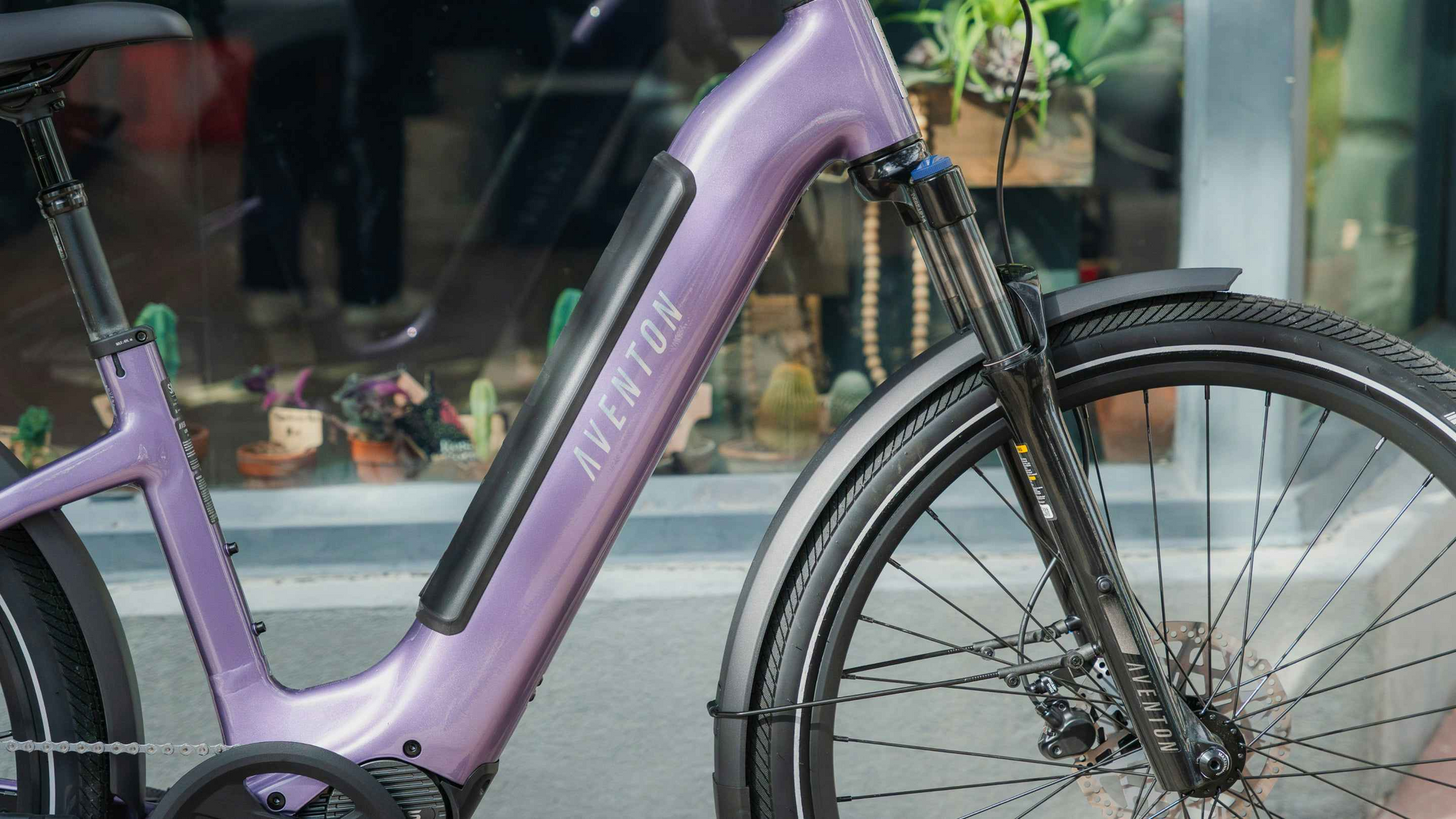 Close-up of the Aventon Level 4 ADV eBike by Aventon, featuring a purple frame, integrated battery, front suspension fork, and a front wheel with disc brake.