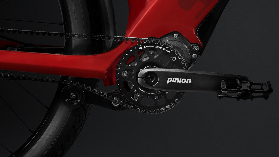 Close-up of a red Stromer ST3 Pinion Launch Edition bicycle's black crankset and pedal, prominently displaying the 'pinion' logo on the crank arm, set against a dark background.