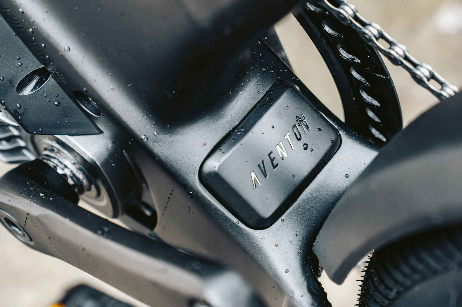 Close-up of a wet Aventon Level 4 ADV eBike frame by Aventon, showing the embossed "AVENTON" logo near the chain and crank area.