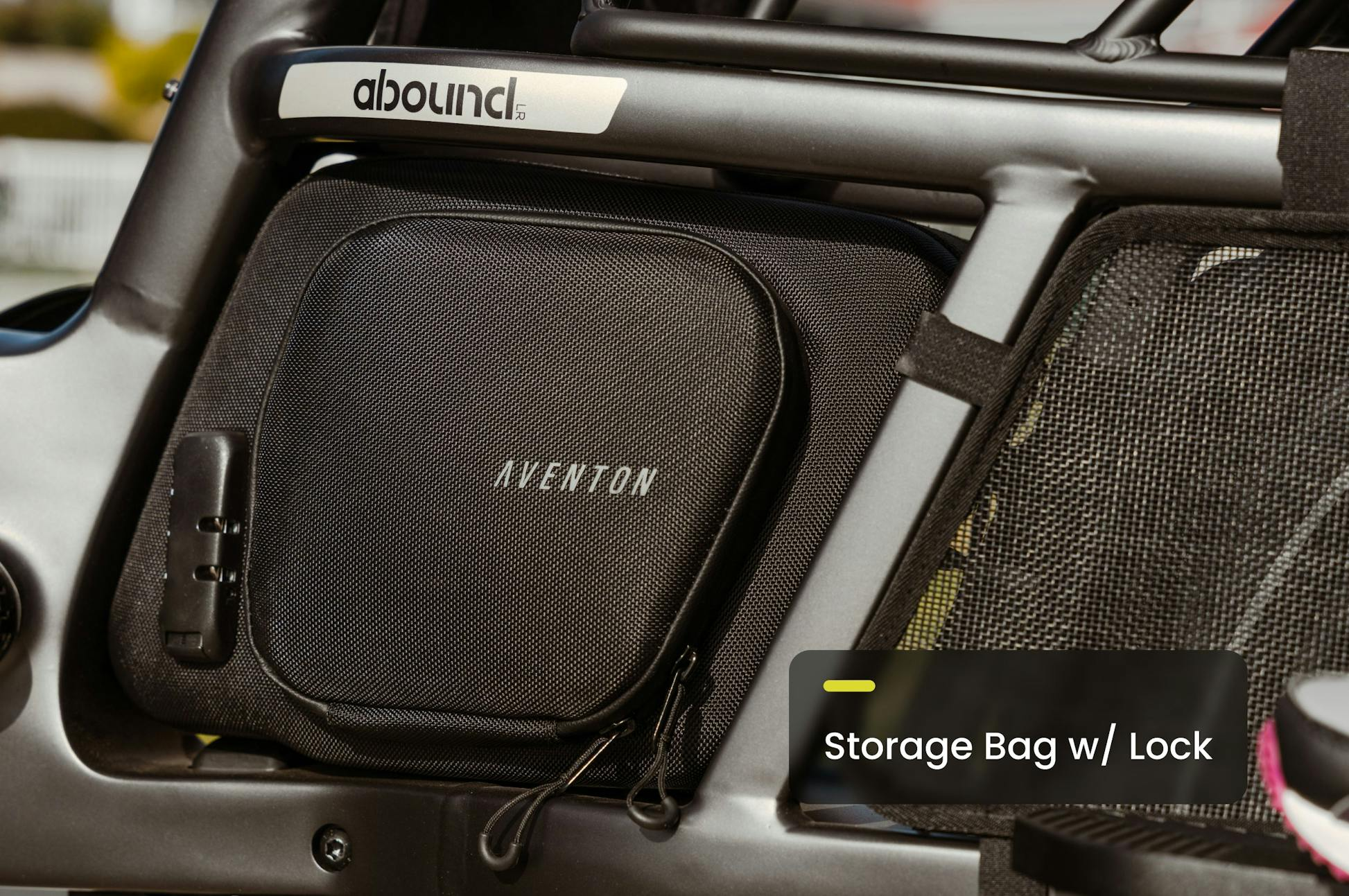 Close-up of a black Aventon storage bag with lock on the frame of an Aventon Abound LR electric cargo bike. The label reads "Storage Bag w/ Lock.