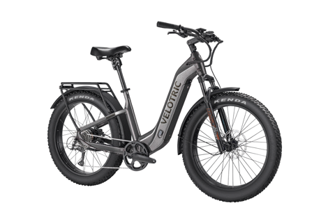 The Velotric - Nomad 2 is an all-terrain eBike in gray, featuring fat tires, a step-through frame, and a rear rack, making it ideal for adventure enthusiasts.