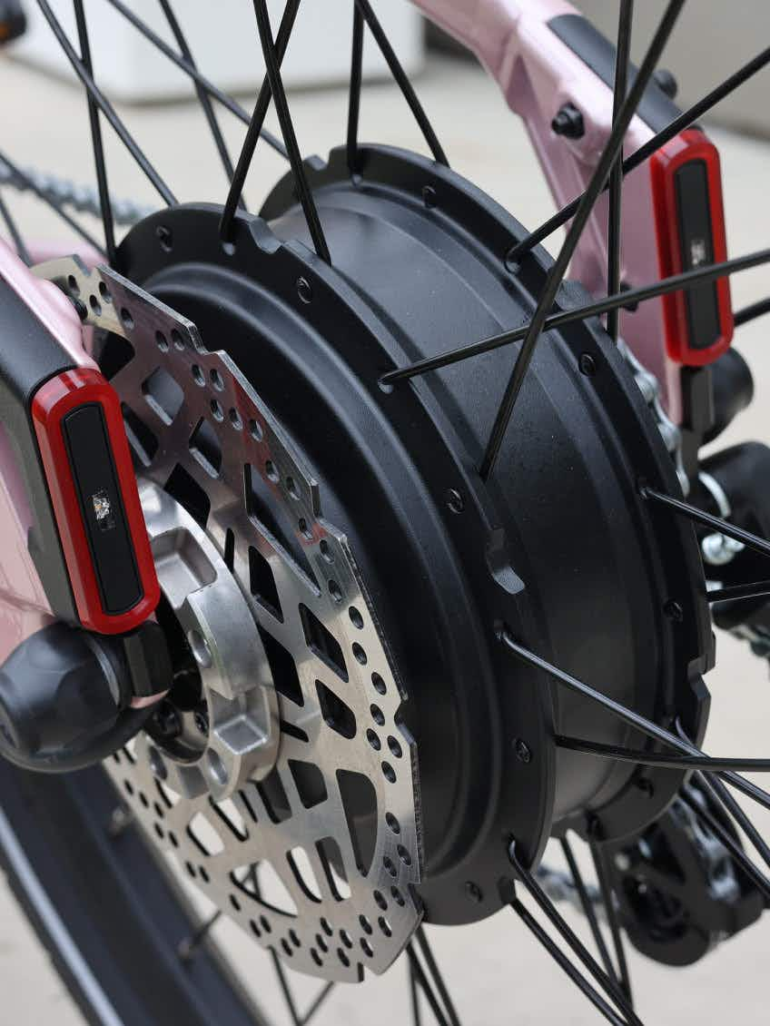 Close-up of the Aventon Pace 5 REC Step-Through electric bike’s wheel by Aventon, showing its disc brake, black motor hub, metal spokes, and red reflectors.