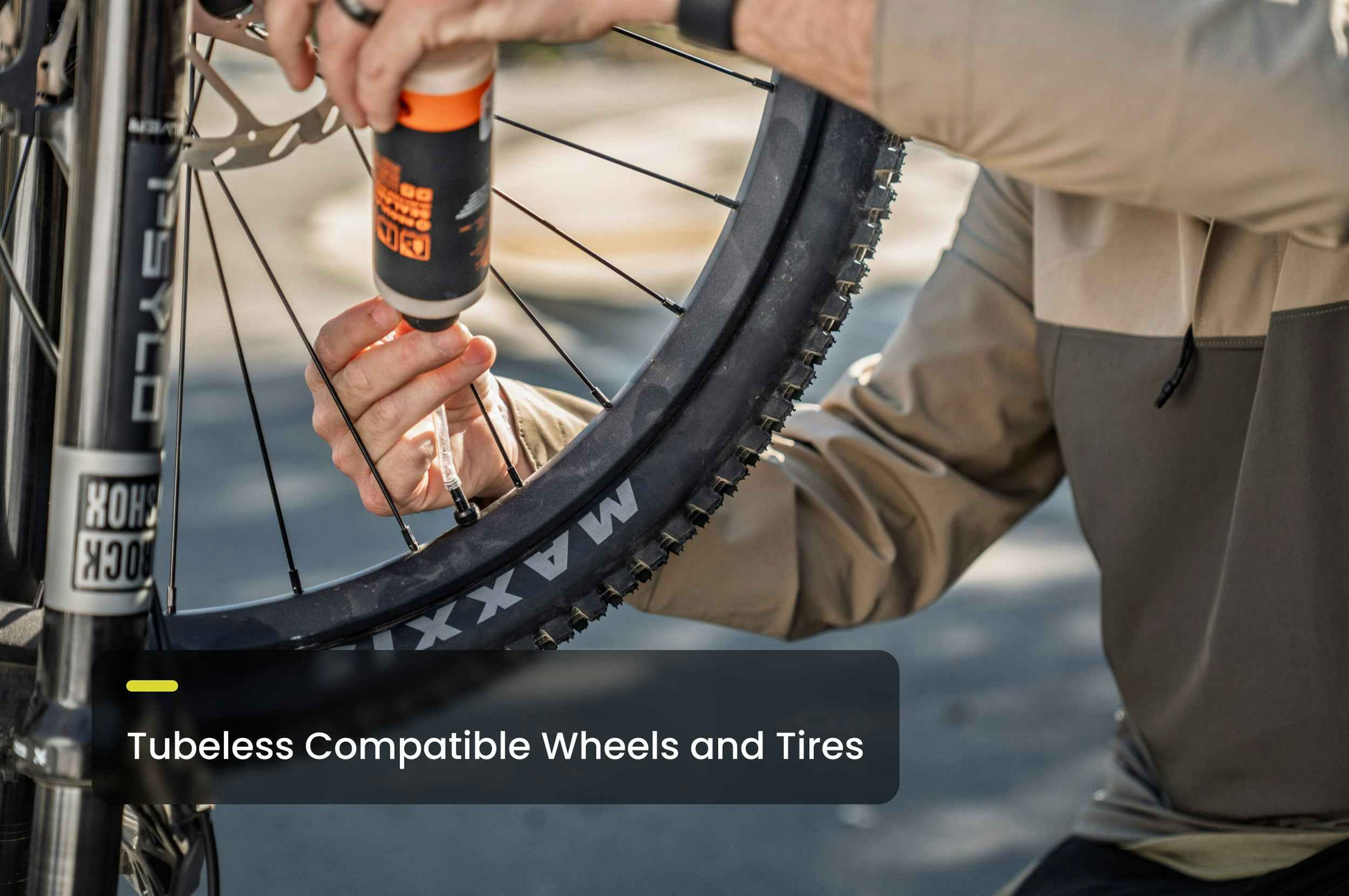 A person applies sealant to the valve of an Aventon Ramblas ADV electric mountain bike wheel labeled "MAXXIS," with the text "Tubeless Compatible Wheels and Tires" overlaid.