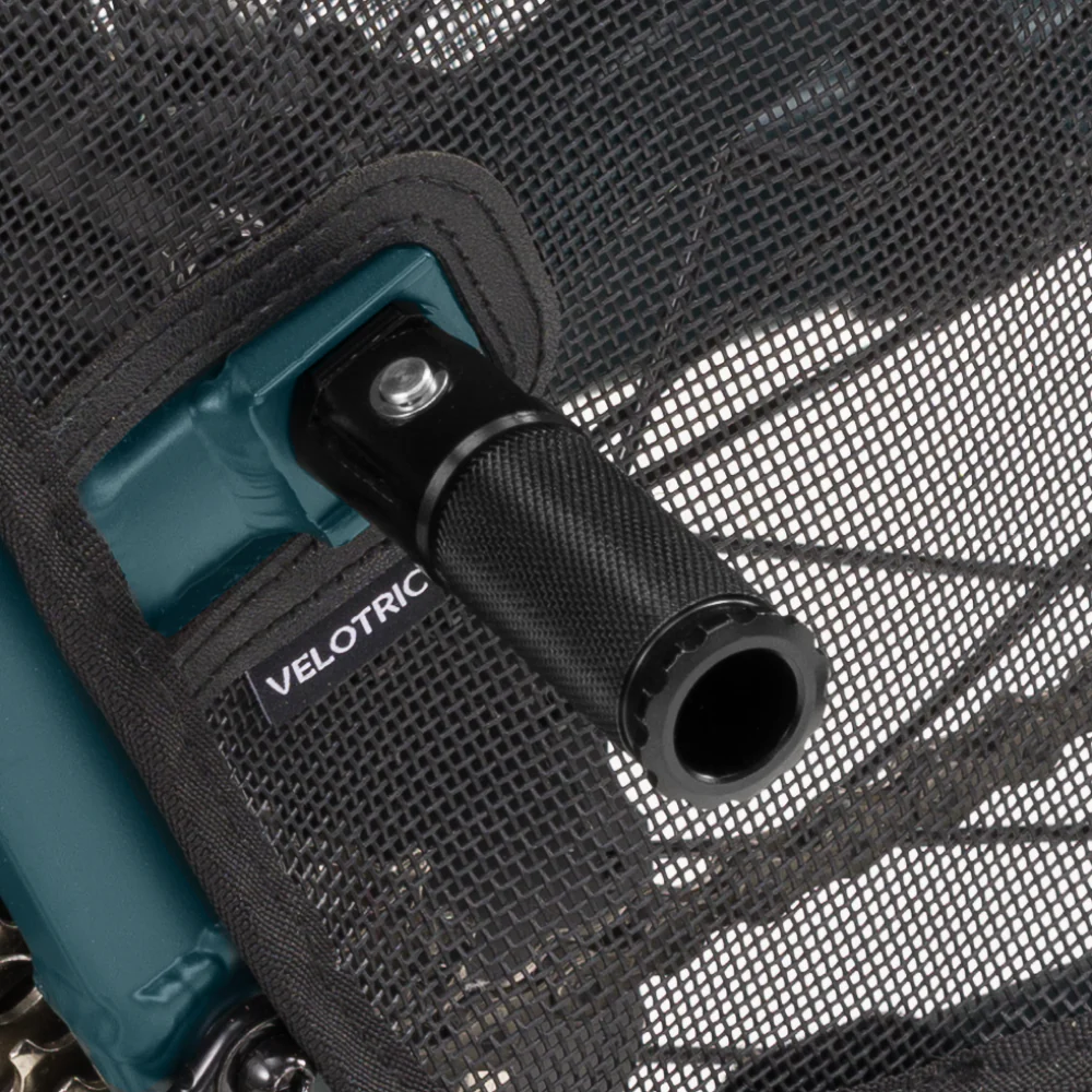 Close-up of a black throttle lever with the brand name "Velotric" on a mesh background, attached to a teal bicycle frame, featuring Rear Pegs - Velotric Go / Fold for added convenience.