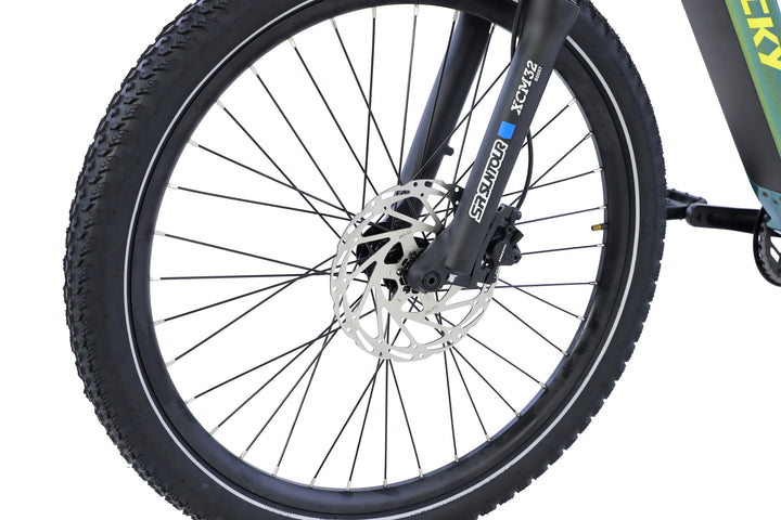 Close-up of the AIMA - Rocky electric bike’s front wheel by AIMA, highlighting its rugged spokes, tire tread, disc brake, and front suspension fork.