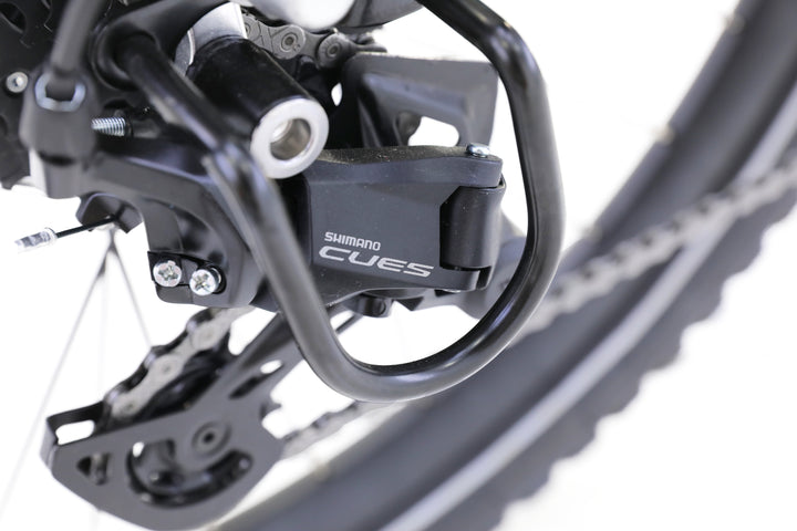 Close-up of the AIMA - Rocky e-bike by AIMA, showcasing the Shimano CUES rear derailleur, drivetrain, and part of the rear wheel for trail-ready performance.
