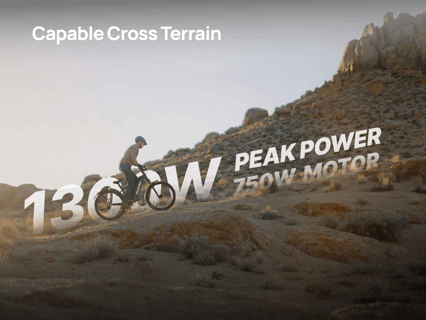 A rider climbs a rocky hill on the Velotric Summit 2, with on-screen text reading "1300W Peak Power 750W Motor" and the phrase "Capable Cross Terrain.