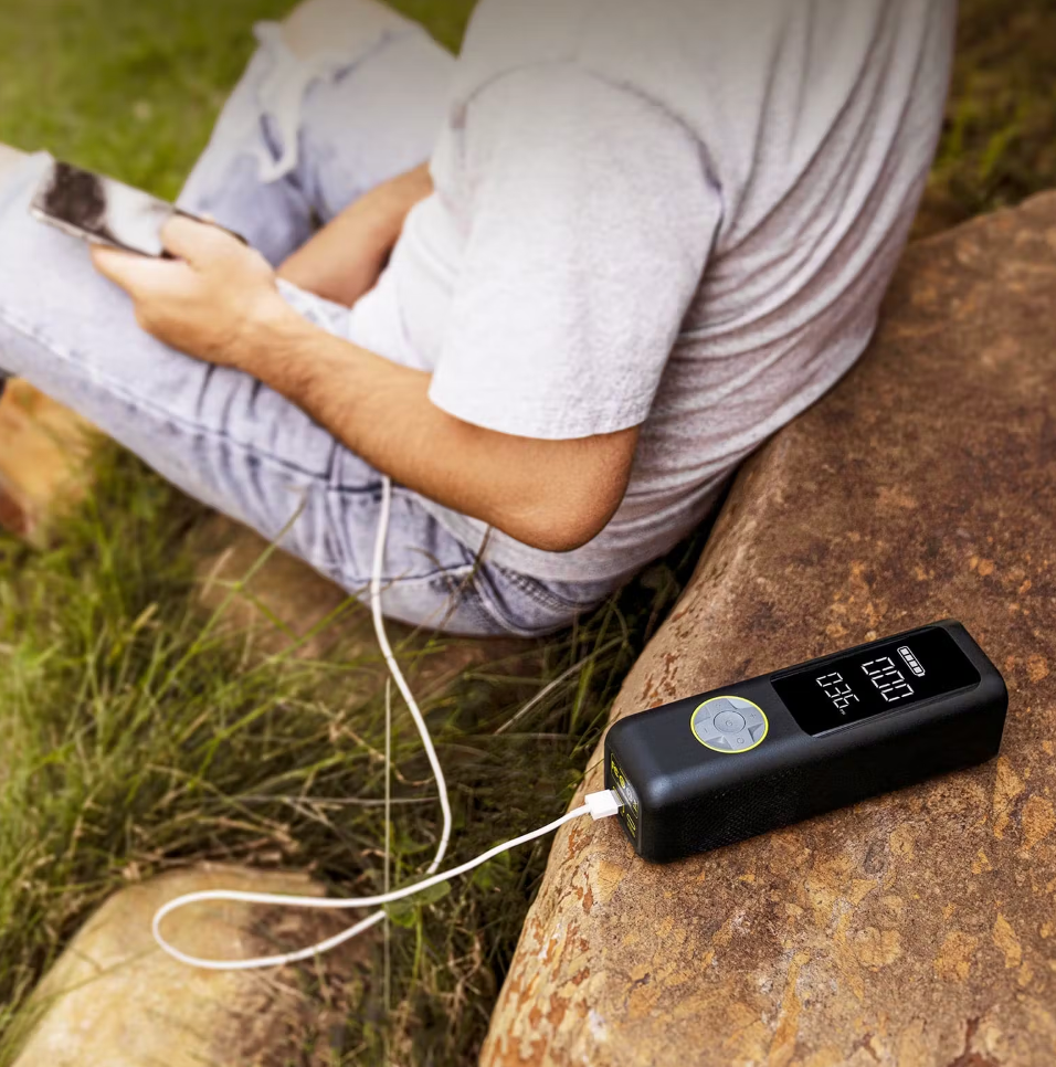 Person sitting outdoors, charging a smartphone with a Tampa Bay eBikes portable black battery pack, resting against a rock.