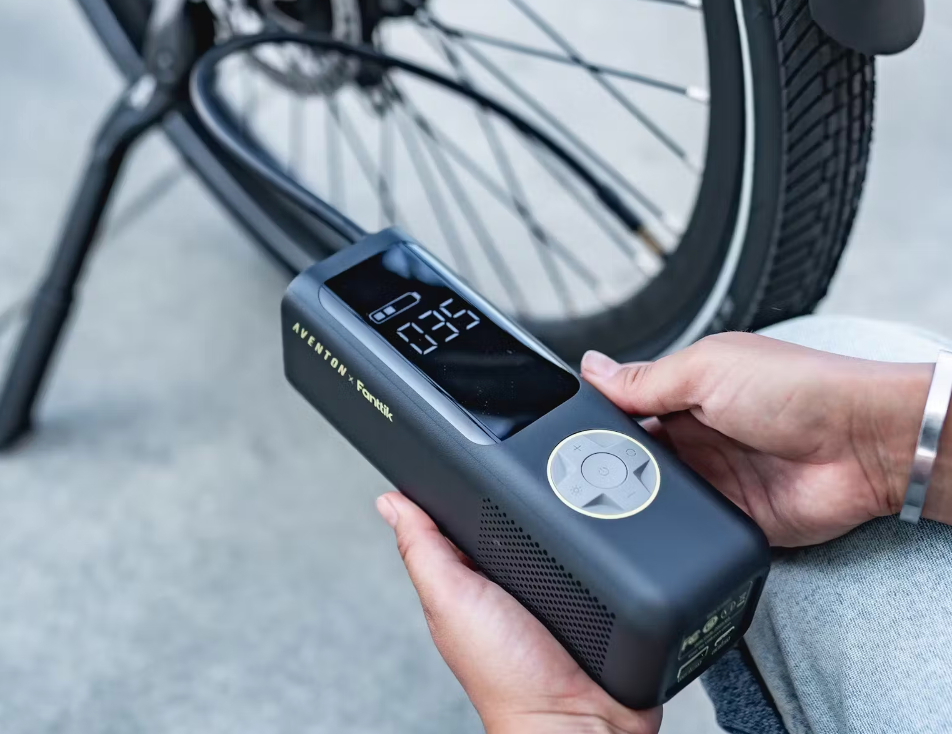 A person holding a Tampa Bay eBikes portable air pump near a bicycle tire, displaying a pressure reading of 26.5 psi on the digital screen.