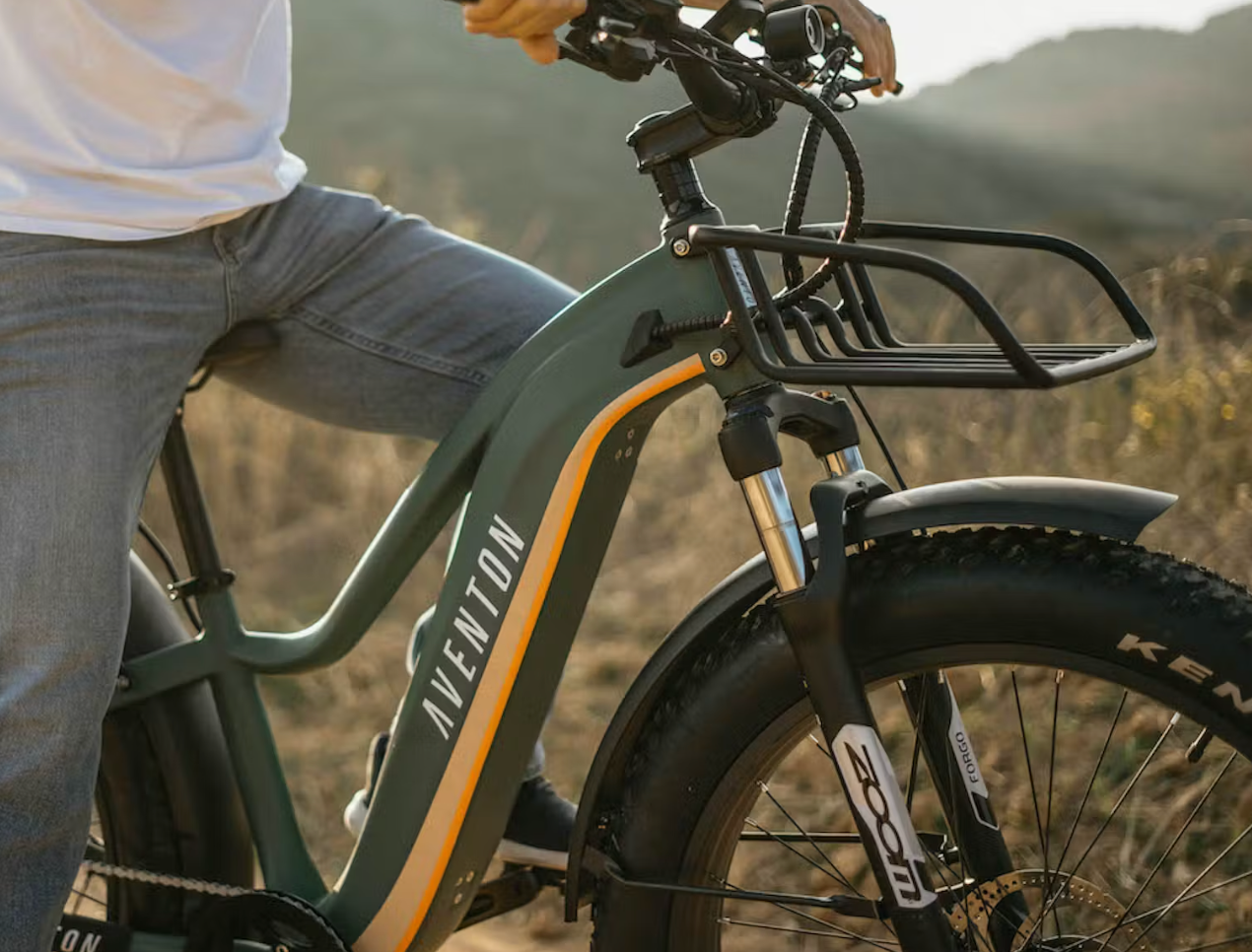 Person leaning on an Aventon Aventure fat tire eBike outdoors, focusing on the bike's frame and handlebars.