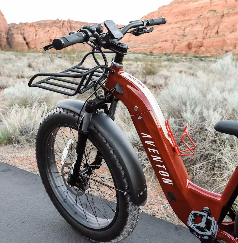 Close-up of a red Aventon Aventure electric bike with fat tires, parked against a rocky desert backdrop showcasing the Front Rack - Aventon Aventure.