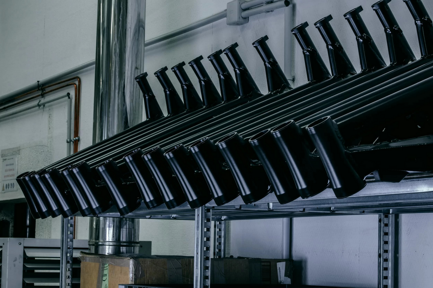 Several black metal pipes are arranged in an angled rack on a shelf within an industrial setting, much like the precision organization you'd find at LMX, where every part of the LMX - 64, from pedal assistance to brushless mid-mounted motors, has its place.