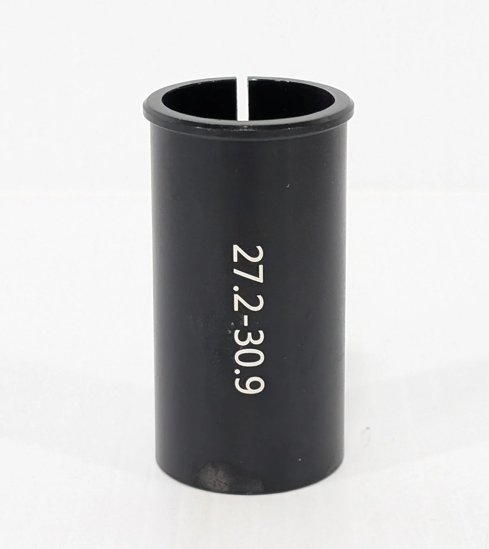 A black cylindrical "Bikase Seat Post Shim" from BiKASE, with white text "27.2-30.9," stands on a pristine white surface—a sleek bicycle accessory designed for precision and performance.