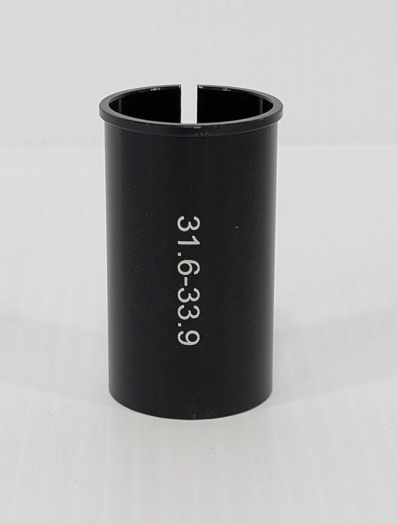 A black cylindrical object with "31.6-33.9" on its side, standing upright on a white surface, is the Bikase Seat Post Shim from BiKASE—a practical bicycle accessory.