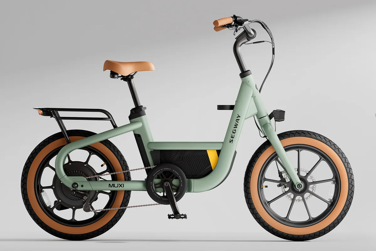 A matte green Segway Muxi electric bike by Segway features a tan seat and grips, black rear rack, and tan-accented tires, displayed in profile on a plain light gray background.