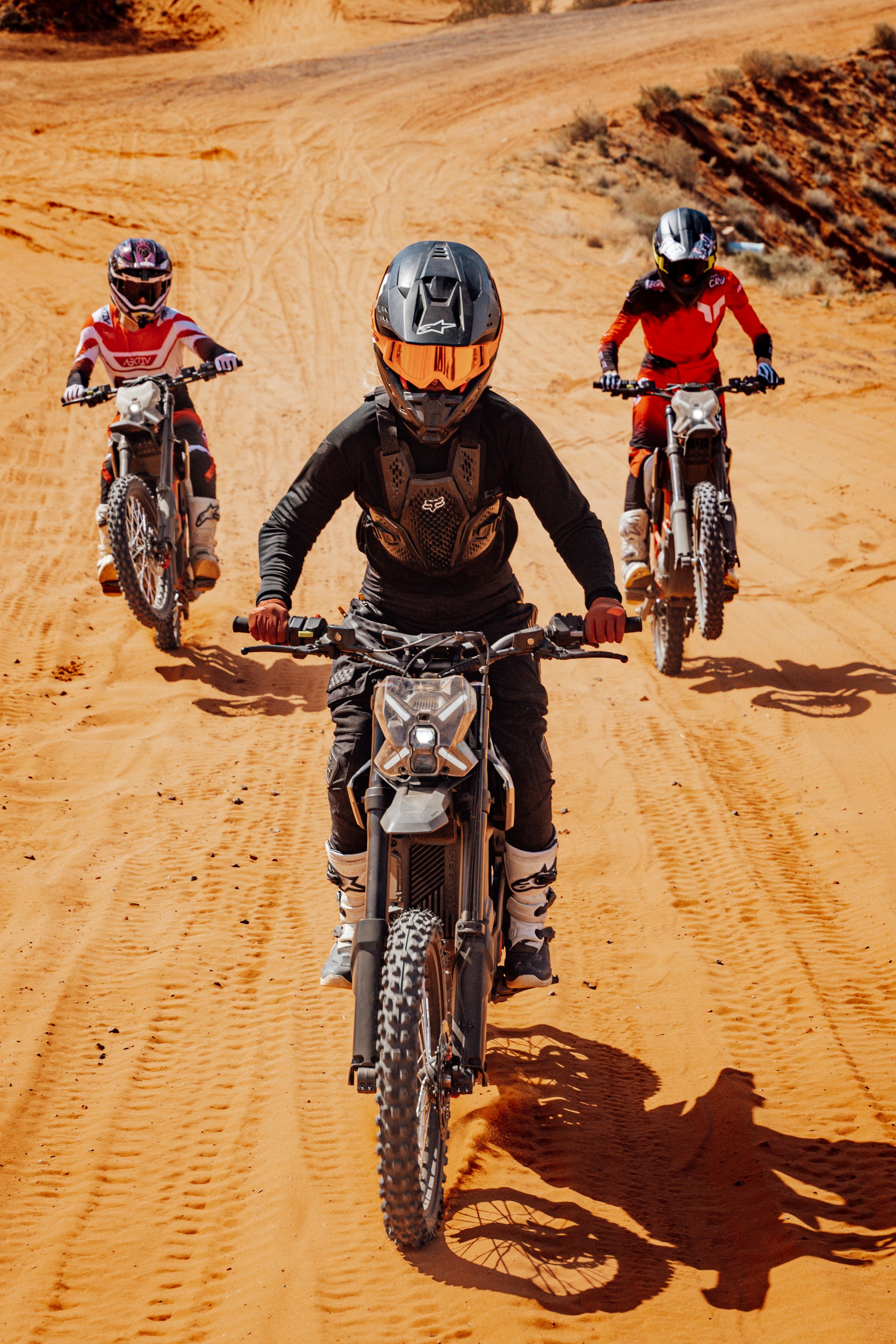 Three riders, equipped with helmets and protective gear, take Segway Xaber 300 electric dirt bikes off-road on a sunny day, highlighting Segway’s powerful performance on sandy trails.