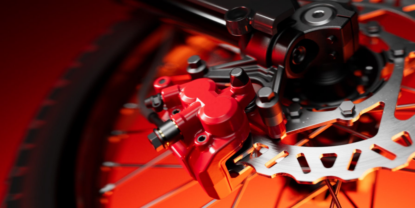 Close-up of a red hydraulic disc brake caliper mounted on an electric dirt bike wheel with a metal rotor and orange lighting, highlighting the high-performance components of the Segway Xaber 300 by Segway.