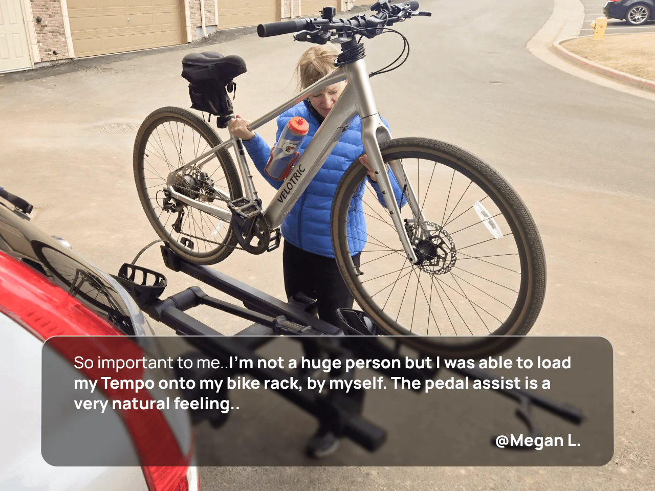 A person loads a Velotric Tempo electric bike by Velotric onto a car bike rack while holding a water bottle in a residential driveway.