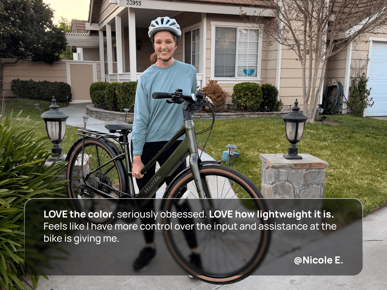 A woman smiles outdoors next to a Velotric Tempo by Velotric, with a residential house and garage in the background.