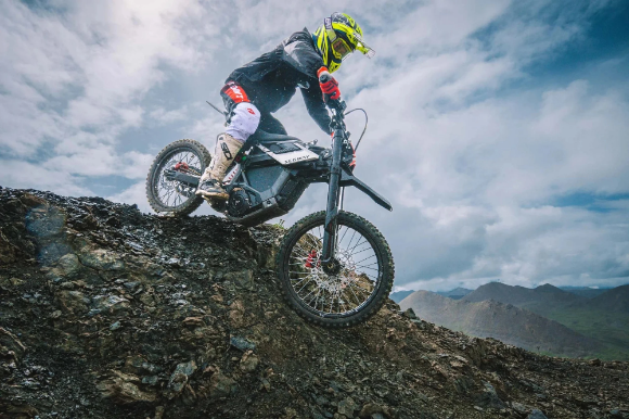 A motorcyclist in protective gear rides the Segway Xaber 300 by Segway down a rocky slope under a cloudy sky, demonstrating the electric dirt bike’s impressive off-road capabilities.
