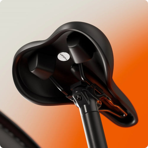 Close-up of the underside of a black seat on the Urtopia Carbon Classic electric bike by Urtopia, attached to its seat post against a blurred orange and white background—highlighting its sleek, lightweight engineering.