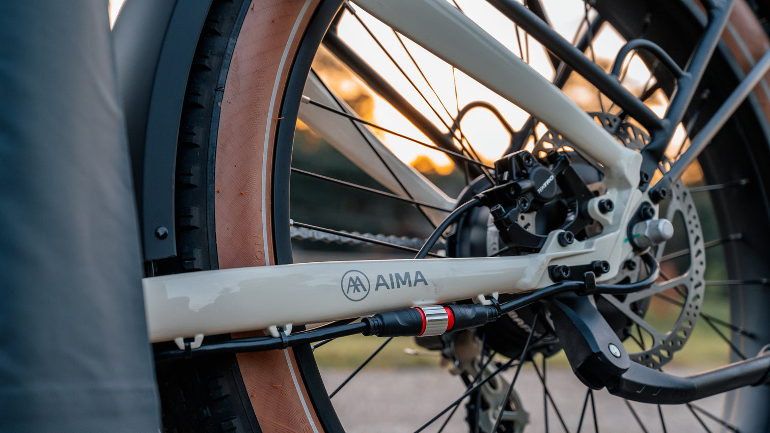 Close-up of the rear wheel and frame on the AIMA - Big Sur eBike, highlighting its disc brake and part of the chain mechanism. The all-terrain frame, marked "AIMA," suggests the robust motor inside, prepared to handle any trail.