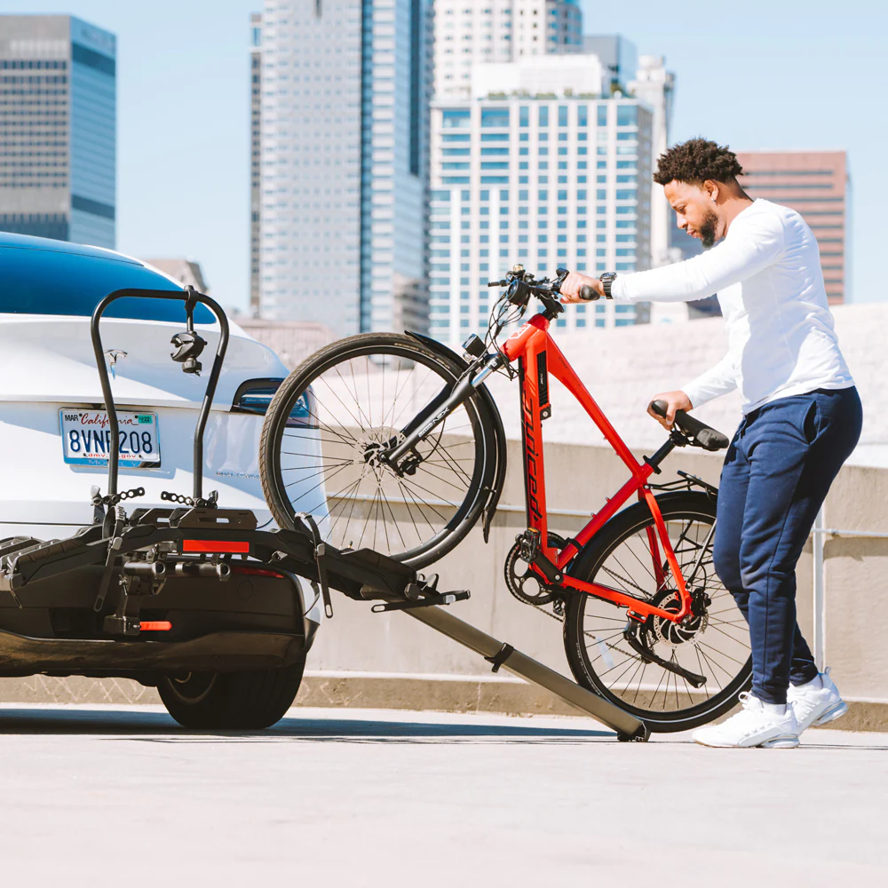 A man utilizing a Hollywood Racks - Destination eBike Rack to load an electric bike onto the back of a car.