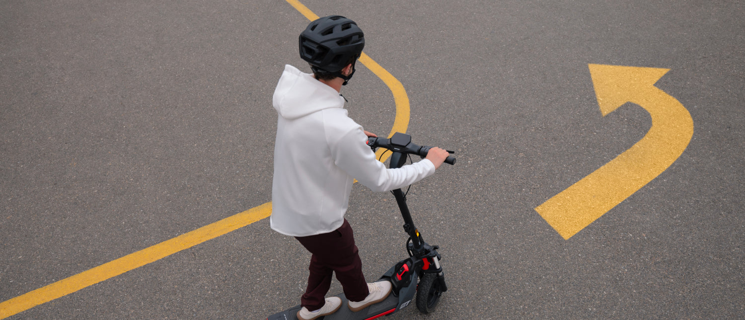 A person in a white hoodie and black helmet glides effortlessly on a Segway ZT3 Pro with advanced suspension, cruising down the paved road marked by a large painted yellow arrow.