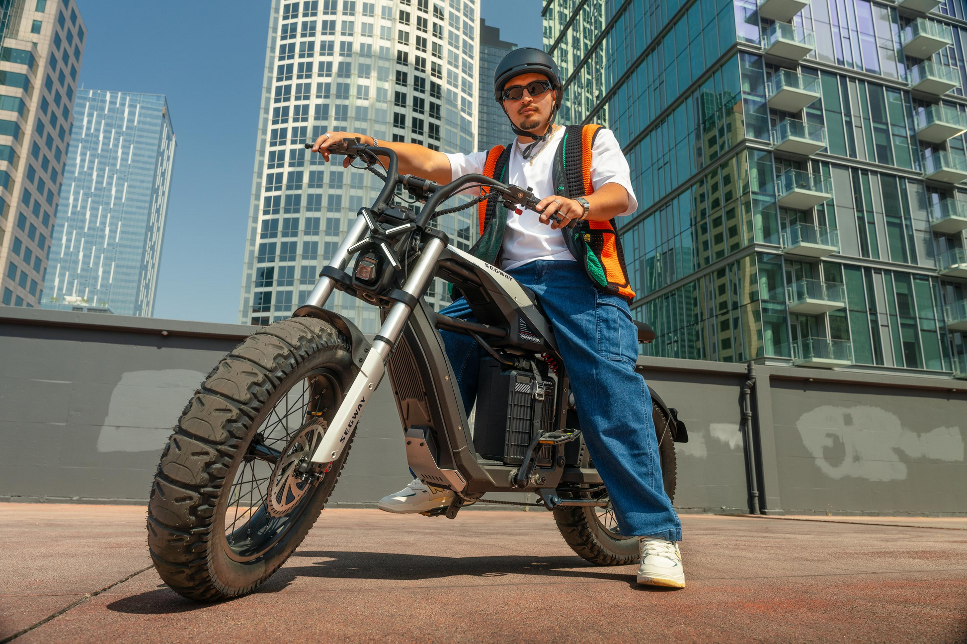 Clad in a safety vest and jeans, a person confidently sits on the high-performance Segway Xyber eBike, helmet and sunglasses on. With towering Tampa Bay skyscrapers as their backdrop, they're geared up for an exhilarating urban adventure.