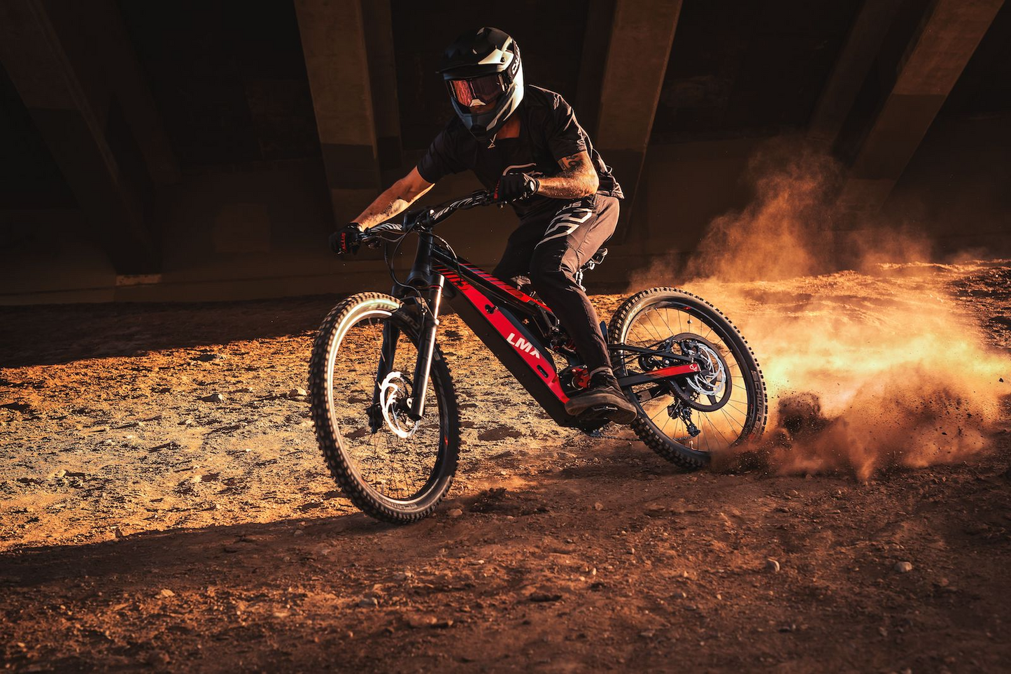 A person wearing protective gear rides a red mountain bike with pedal assistance through a dusty trail under a bridge, showcasing the capabilities of the LMX - 64 from LMX.